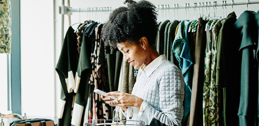 Woman smiling and looking down at her phone while in a clothes shop